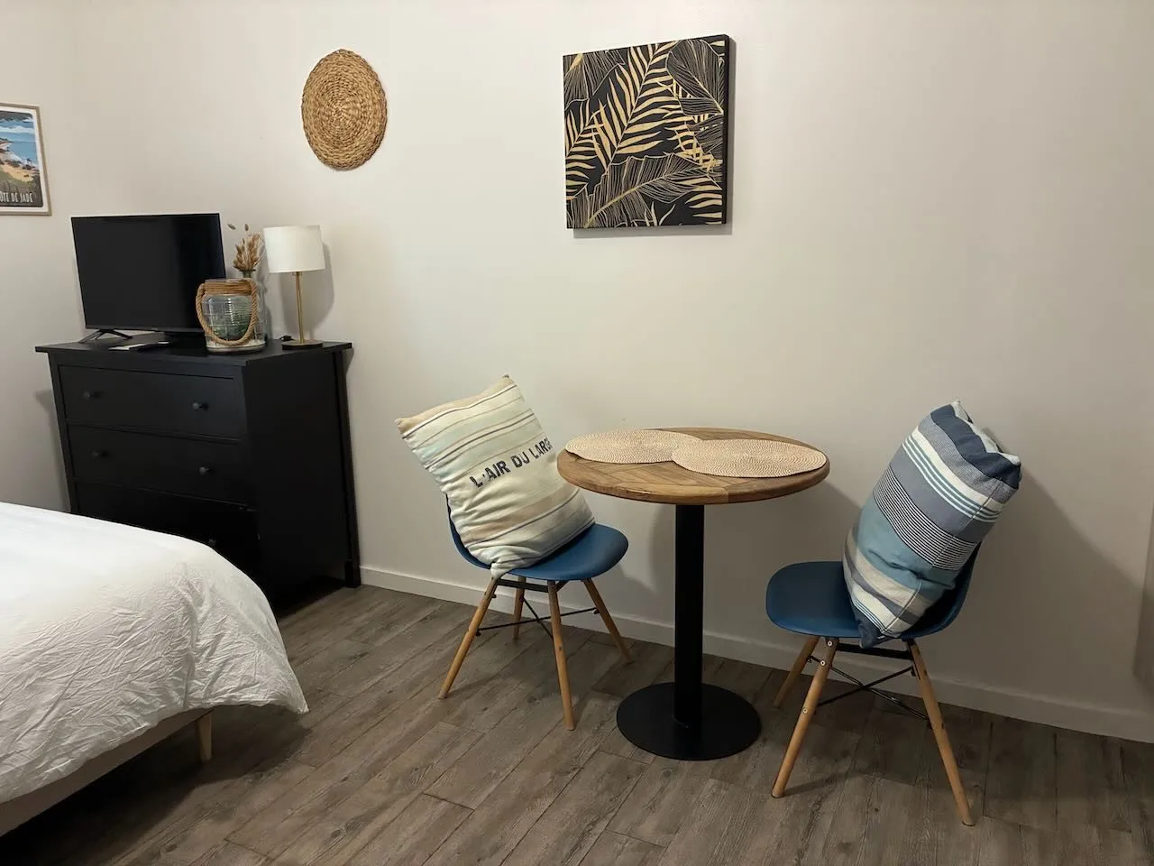 Coin repas avec sa table ronde en bois, deux chaises bleues et la télévision sur la commode