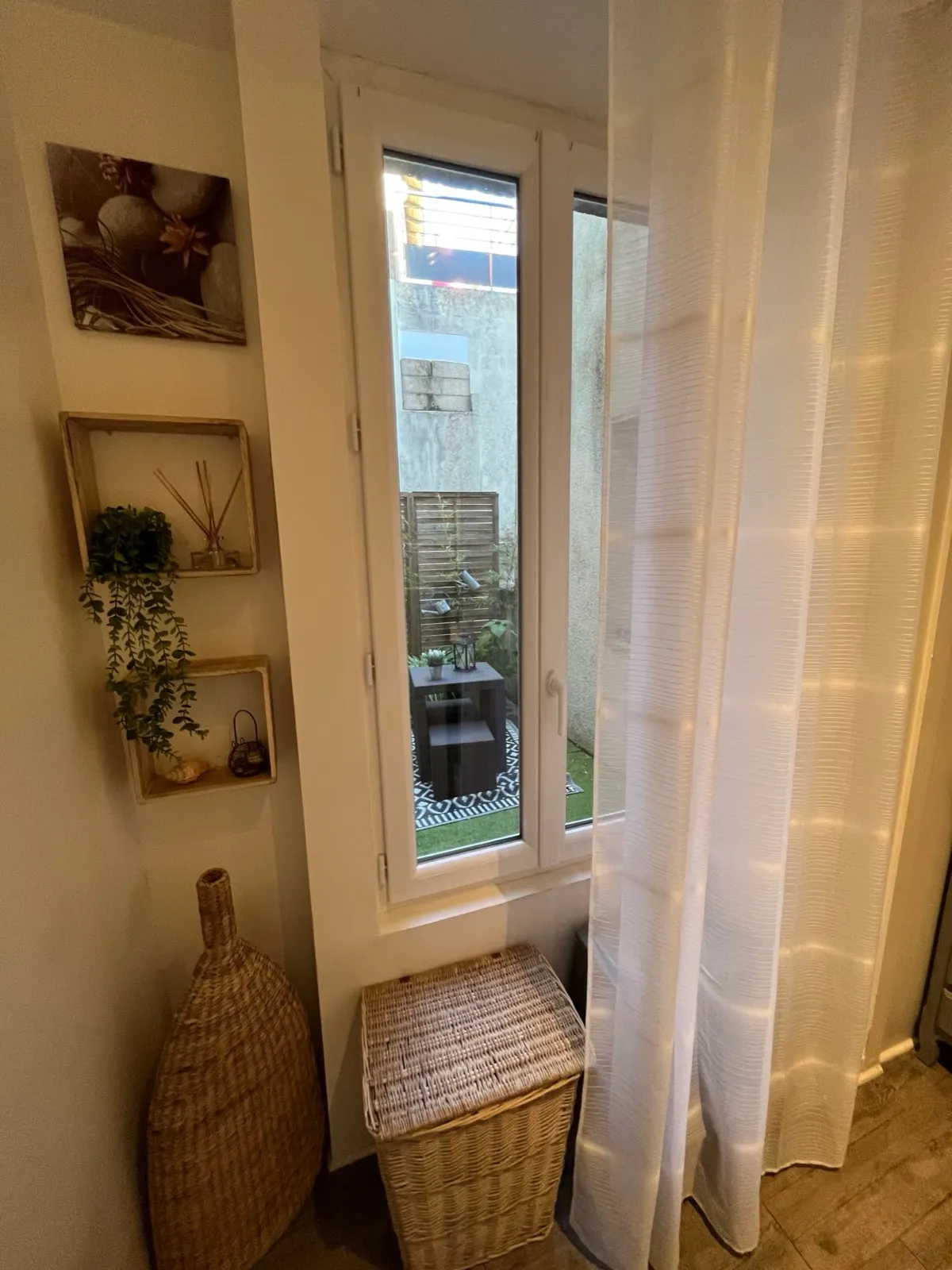 Salle de douche avec sa porte-fenêtre donnant sur le patio, panier en osier et étagères déco