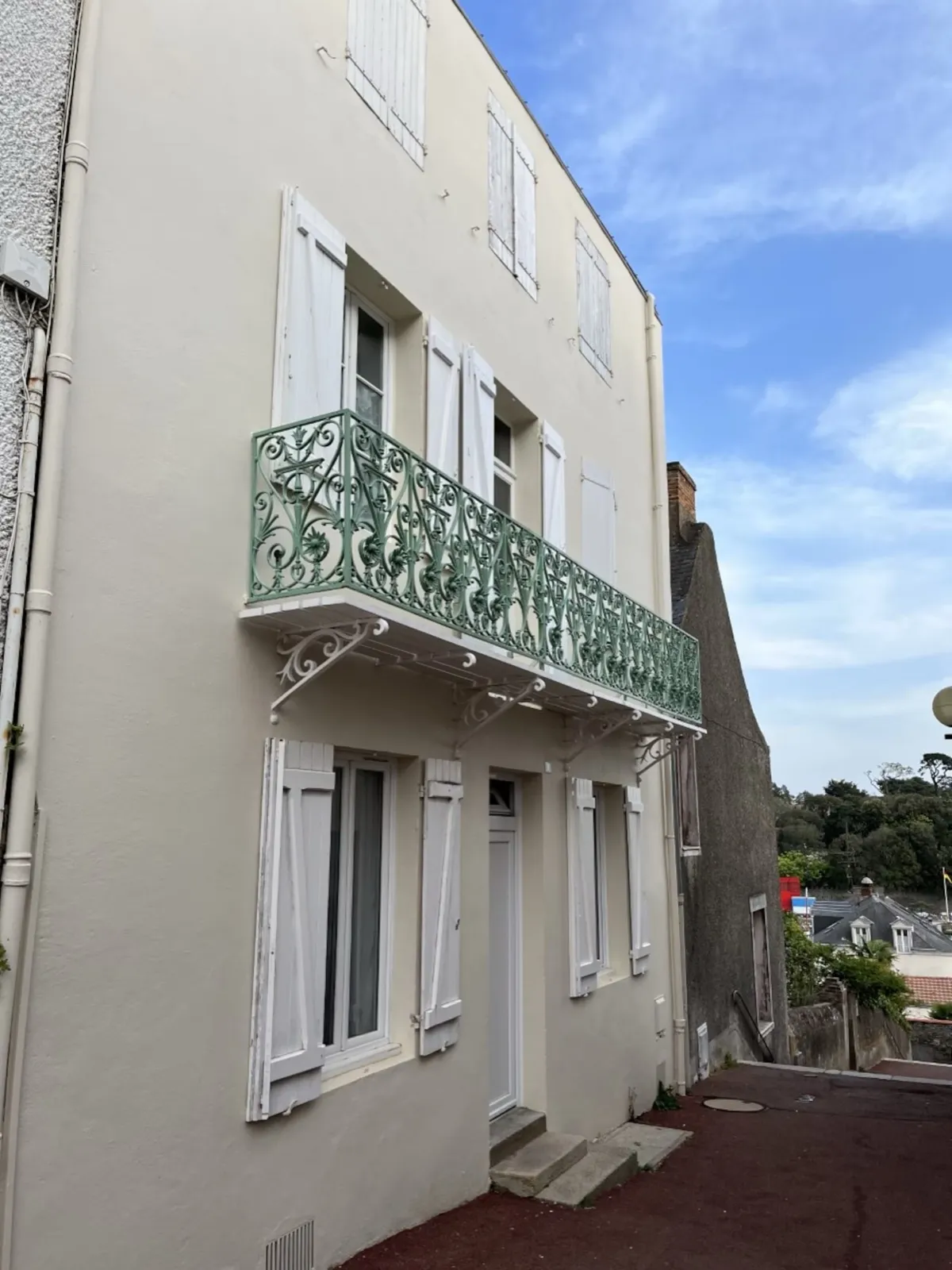 Façade de l’immeuble, balcon en fer forgé vert et volets blancs, escalier Galipaud à Pornic